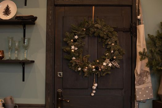 Close-up of fir tree Christmas wreath with decorations hanging on dark brown wooden front door of a house. Decorated Christmas wreath on the front door.