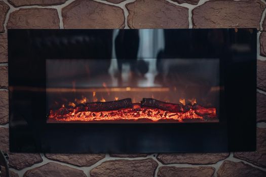 Close-up of stony fireplace with burning or smoldering logs on fire.