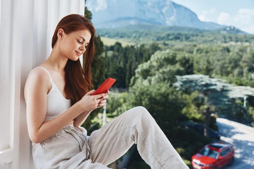 pretty woman sitting on the balcony with phone beautiful mountain view summer Perfect sunny morning. High quality photo