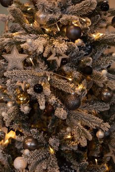 Close-up of beautiful snowed Christmas tree with garland and decorative balls and stars.