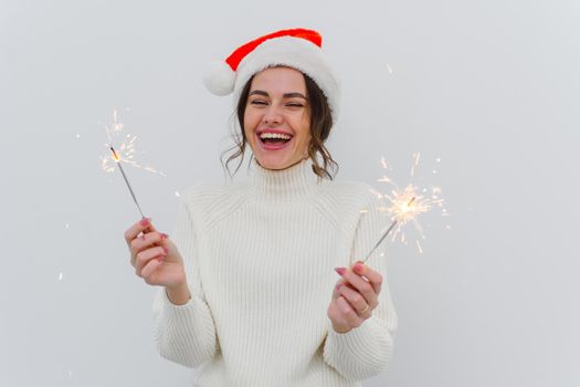 Lovely young woman in white sweater holds sparklers and laughs, smiles with a wide smile