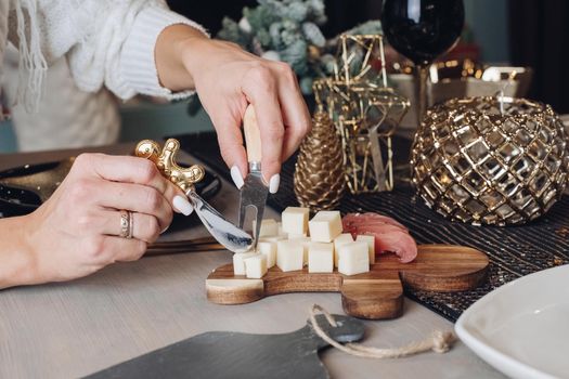 Cropped photo of woman tasting cheese on a wooden board with Christmas decorations in the background