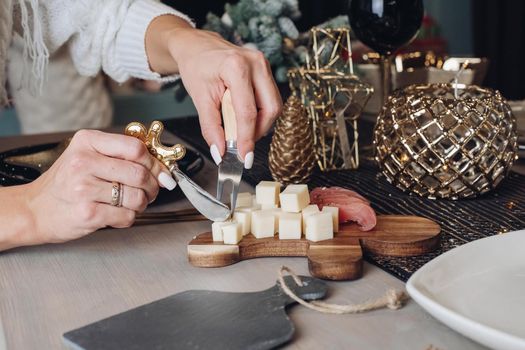 Cropped photo of woman tasting cheese on a wooden board with Christmas decorations in the background