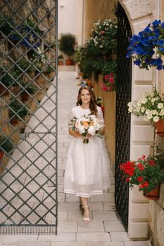 Bride with a bouquet of flowers comes out of an old courtyard with a decorative gate. High quality photo