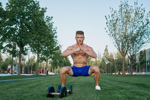 Muscled man in the park training with dumbbells. High quality photo