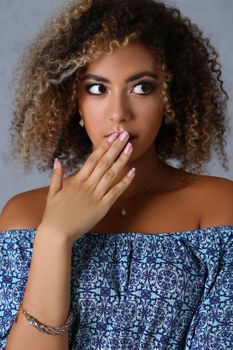 Portrait of beautiful latin young woman with shocked or surprised facial expression close mouth with hand. Curly hair and stylish outfit. Model concept