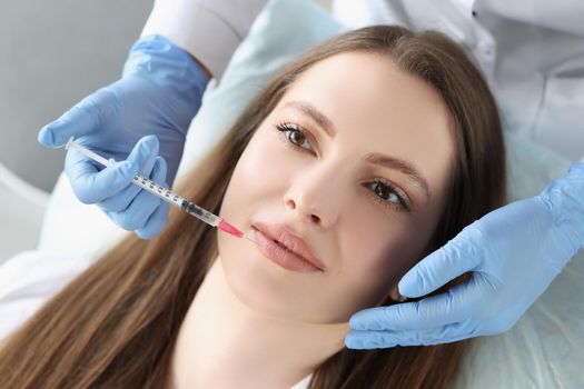 Portrait of young woman gets injection of botox in her lips, cosmetologist using syringe. Cosmetology, beauty treatment, plastic surgery, clinic concept