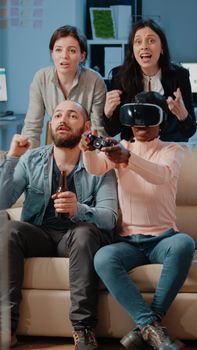 Multi ethnic people cheering while woman winning game with vr glasses and controller on tv console. Workmates enjoying video games with joystick to have fun with activity after work