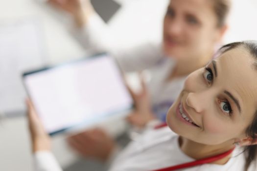 Top view of women working in hospital spend pause with tablet device. Smiling nurse hold gadget with white screen. Pause from work, pastime, clinic concept