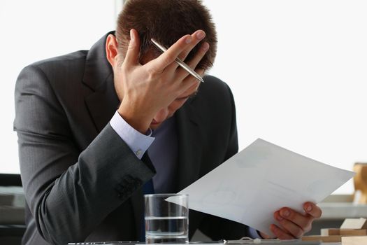 Close-up of adult man businessman hold paper sheet in hand and close face with palm. Wrong financial calculations led to failure. Business strategy concept