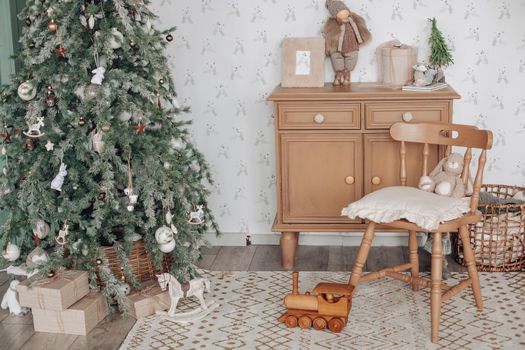 View over white modern room decorated for Christmas holidays. Decorated and illuminated Christmas tree, fireplace with fir branch, candles and handmade paper stars in fireplace.