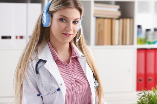 Portrait of pretty female blonde doctor talking to patient over wireless headset advises medical problem. Remote education, internship, callcenter concept