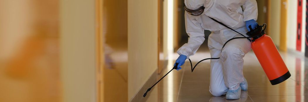 Specialist in protective suit and mask disinfects corridors. Treatment of premises in an epidemic concept