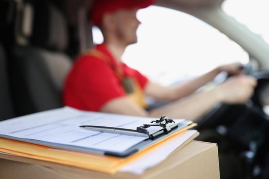 Close-up of docs on box and smiling courier deliver packages to people on car. Worker in special red uniform. Delivery service, shipping, transfer concept