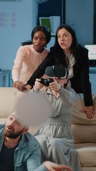 Cheerful colleagues having fun with video games after work, using vr glasses to play on tv console. Workmates playing game with controller and virtual reality headset for entertainment