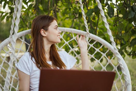 smiling woman outdoors in hammock with laptop technology. High quality photo