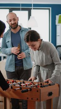 Cheerful women playing at foosball game table after work. Workmates enjoying fun activity with alcoholic drinks, snacks and pizza to celebrate party at office. After hours leisure