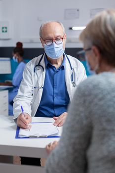 Specialist taking notes on clipboard papers while doing consultation with woman during covid 19 pandemic. Man doctor preparing prescription document for treatment against disease.