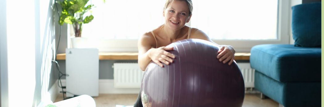 Portrait of happy young woman with large gymnastic ball on rug at home. Fitball exercises at home concept