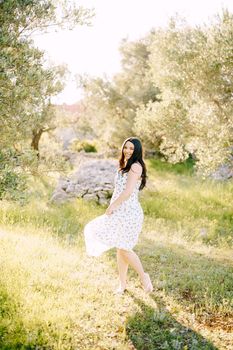 Smiling pregnant woman standing on green grass holding the hem of her dress. High quality photo