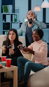 Cheerful coworkers playing video games with joysticks and console on television. Workmates winning game with controllers on tv for entertainment, enjoying drinks and snacks after work