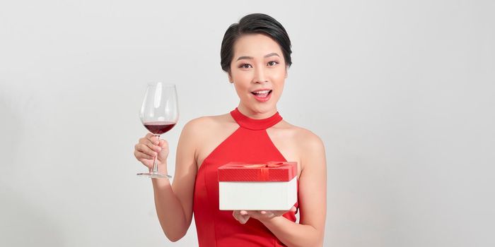 Young attractive woman in evening dress holding gifts red boxes on white background. New Year/Birthday/Anniversary celebration, holiday concept, excitement and admiration