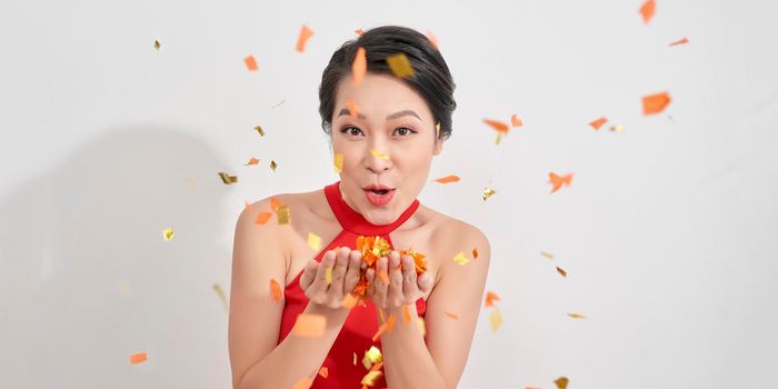 Joyful woman in sundress blows kiss on white background with confetti