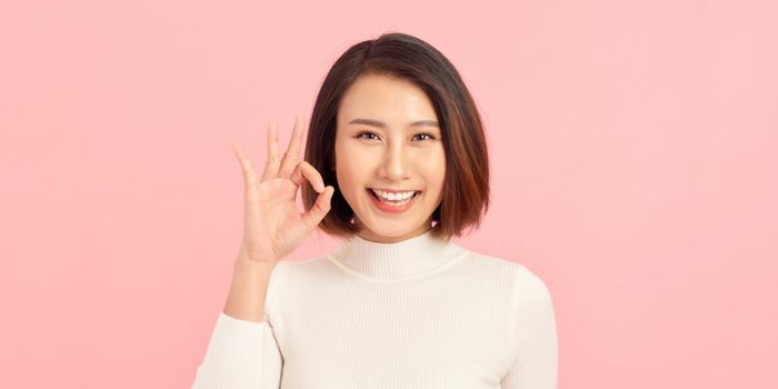 Happy young businesswoman showing ok sign isolated on a pink background
