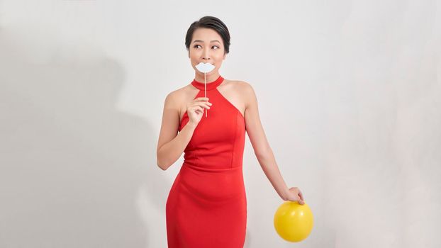 Happy asian woman holding carnival accessories on stick fake silver lips, having fun on white background