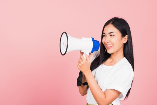 Portrait of happy Asian beautiful young woman teen confident smiling face holding making announcement message shouting screaming in megaphone, studio shot isolated on pink background, with copy space