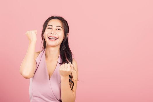 Happy Asian portrait beautiful cute young woman standing winning and surprised excited screaming open mouth raise hands, studio shot isolated pink background, Thai female wow with copy space