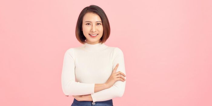 Portrait of a smiling young woman standing with arms folded isolated over pink background