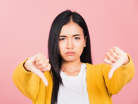 Portrait Asian beautiful young woman unhappy, negative gesture showing finger thumbs down or dislike sign, studio shot isolated on pink background, Thai female rejection unlike with copy space