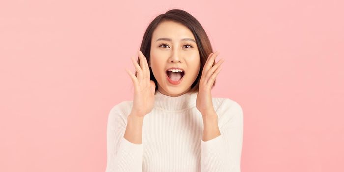 Energetic loud cute beautiful female opening mouth widely, putting hands to mouth, shouting standing isolated over pink background 