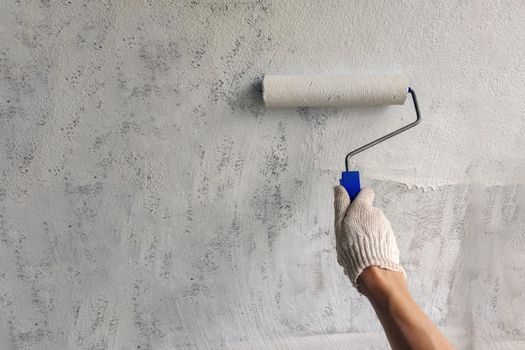 A girl paints a wall with white paint. Hand with roller for painting close up with copy space