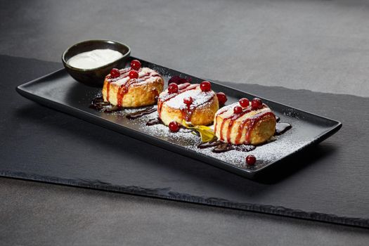 syrniki on a plate with berries and sour cream, front view, dark background