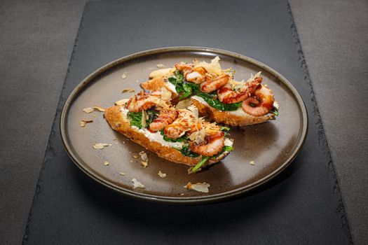 Italian food. Bruschetta with grilled octopuse, spinach and soft cheese. Dark background