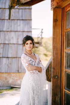 Woman in a white lace dress stands at the door of an old hut. High quality photo