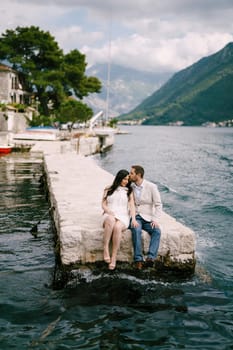 Man kisses woman on the forehead while sitting on the pier by the water. High quality photo
