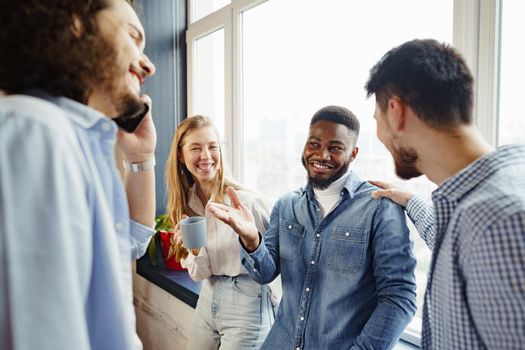 Cheerful young business people have a talk during coffee break in office near window