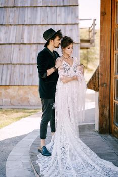 Groom hugs bride in a lace braided dress on the doorstep of a wooden hut. High quality photo