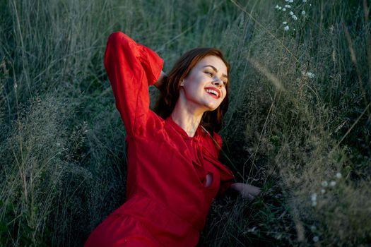 pretty woman in red dress lies on the grass nature sun. High quality photo