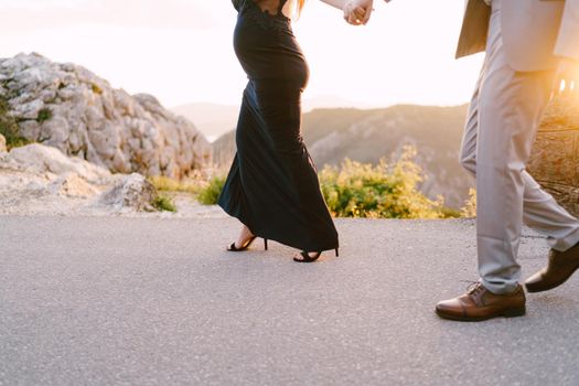 Man and a pregnant woman are walking along an asphalt road in the mountains. Close-up. High quality photo