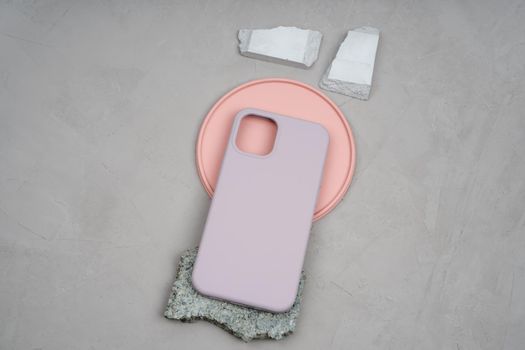 Silicon case for a smartphone lies on a coral round plate of plaster. Different stones by color, size and texture. Pink gypsum plate. Silicone protective case in beige color.