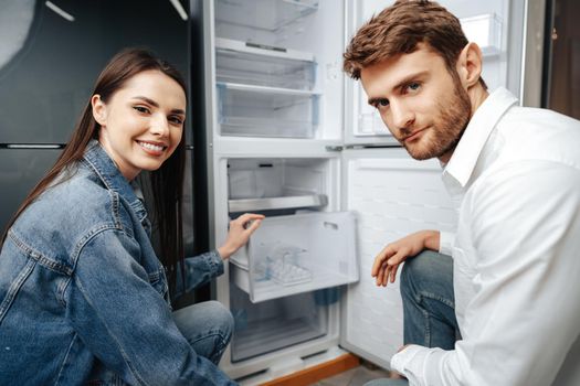 Young couple selecting new refrigerator in household appliance store, close up