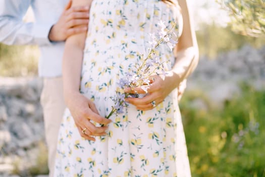 Man hugs pregnant woman holding wildflowers. Close-up. High quality photo
