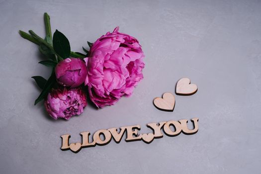 Pink garden peonies on a gray textured background. Wooden inscription I love you. Valentine's Day greeting card. Postcard declaration of love. Wooden decor.