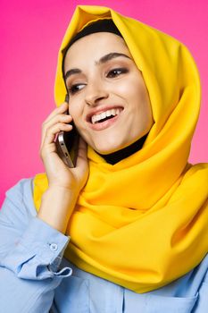 muslim woman in yellow hijab talking on the phone technology pink background. High quality photo