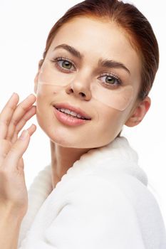 Woman in white robe posing fun skin care patches on face. High quality photo