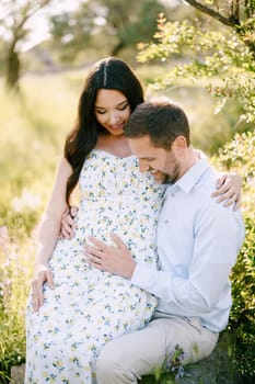 Man holds his hands on the belly of a pregnant woman sitting on his lap. High quality photo